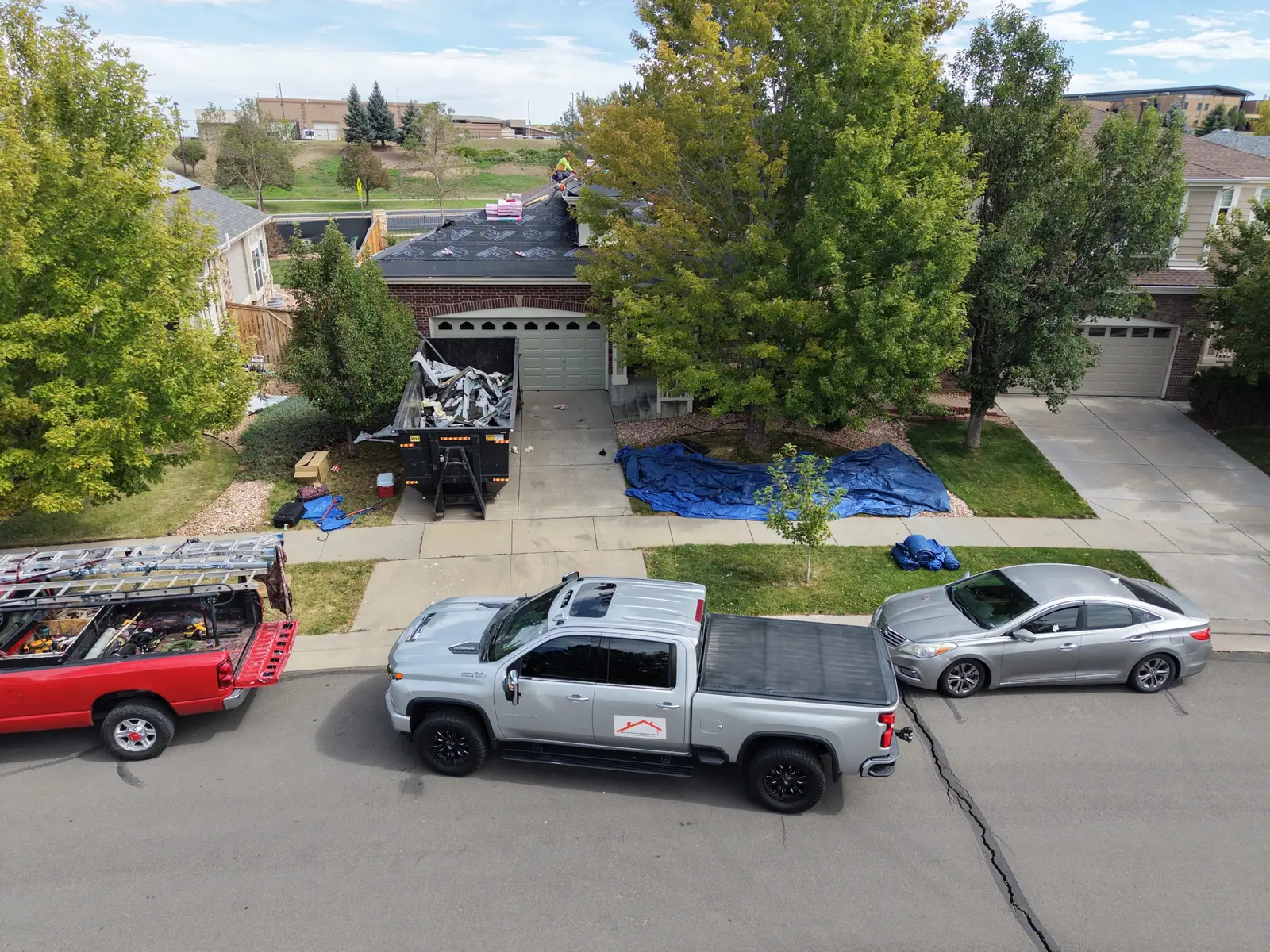 AXEL Roofing pickup at the curb with a dumpster in the driveway and blue tarps over the landscaping