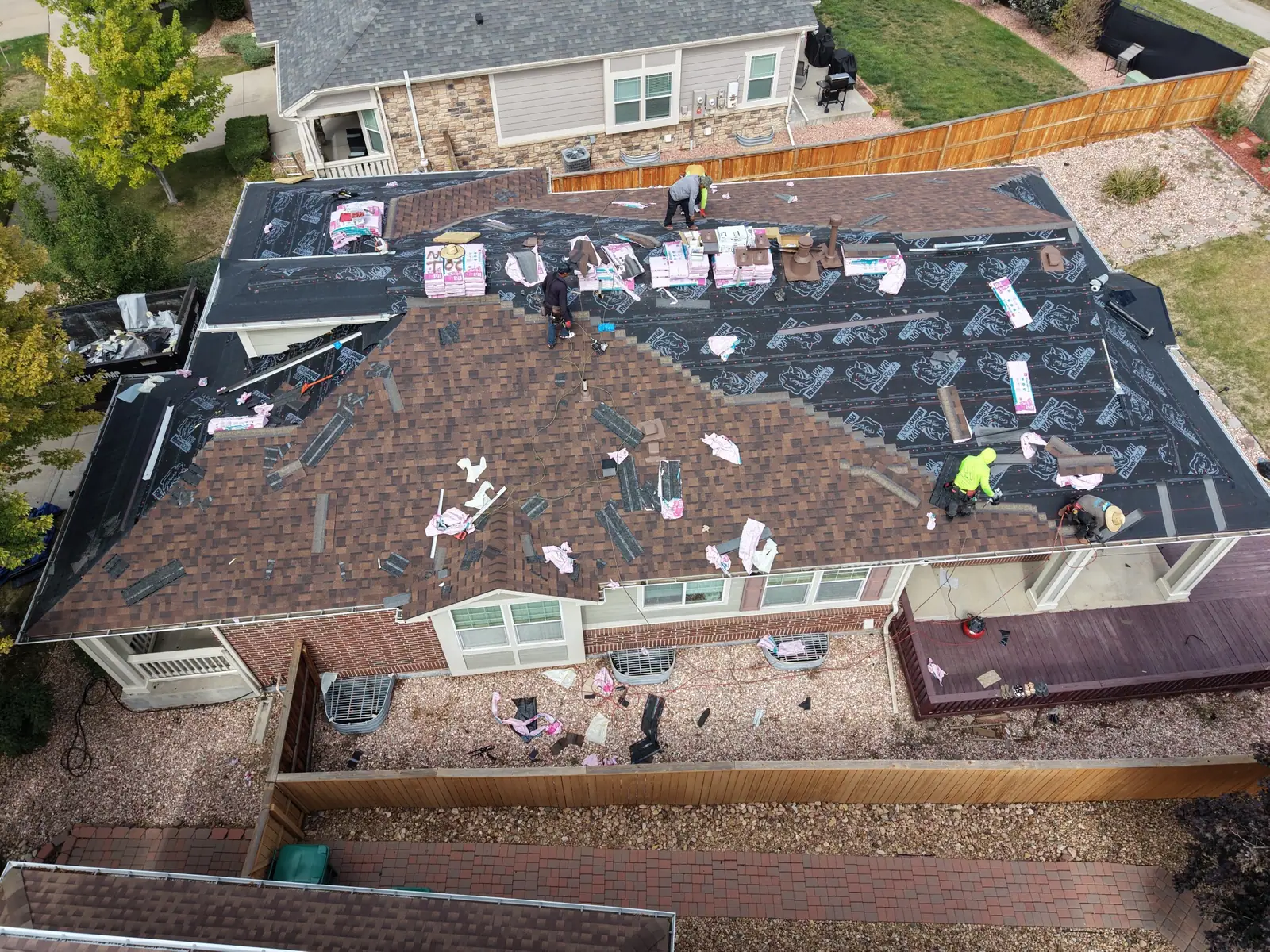Roofers laying new brown architectural shingles across a hip roof on a brick home