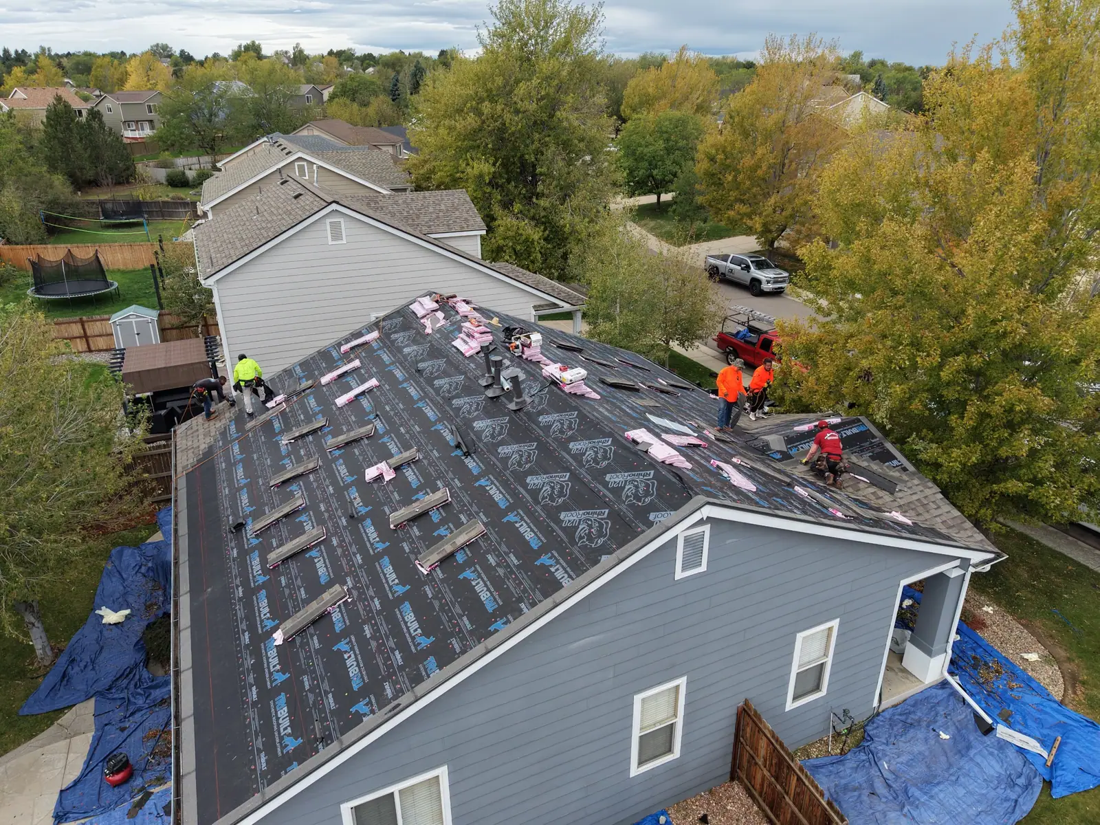 AXEL Roofing crew installing new shingles over synthetic underlayment on a two-story home, tarps protecting the yard