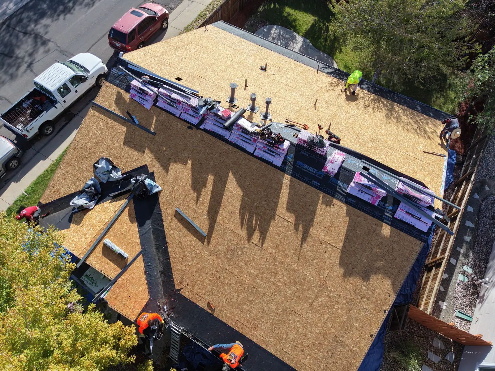 Drone view of an AXEL Roofing crew on a bare roof deck during a full replacement, shingle bundles staged along the ridge