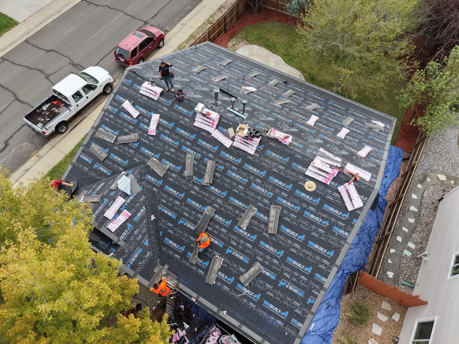 Overhead view of a roof dried in with synthetic underlayment, shingle bundles loaded and roofers starting the field