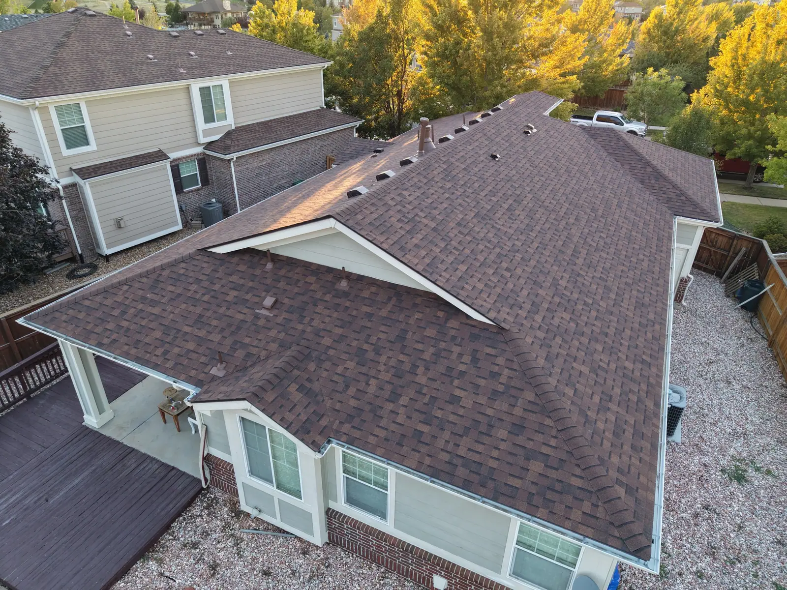 Finished brown architectural shingle roof on a brick and siding home at golden hour, AXEL Roofing job