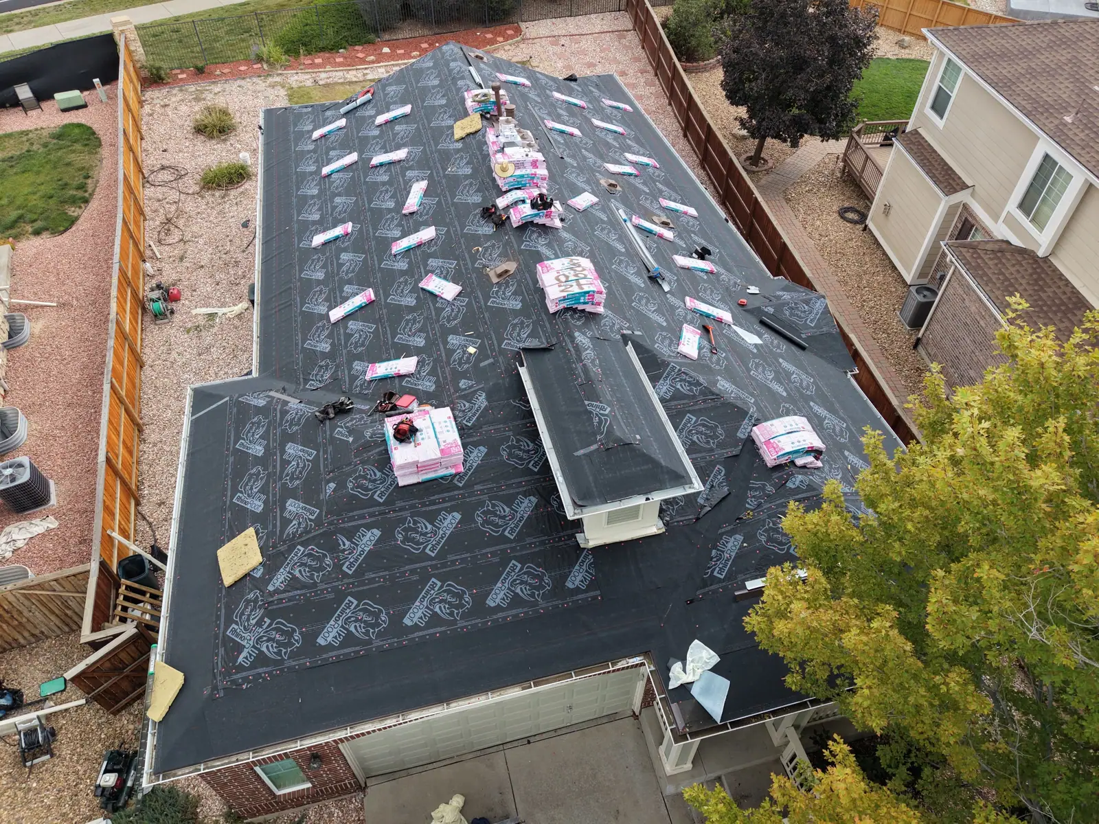 Brick home with the old roof removed and synthetic underlayment covering the deck, bundles staged on the ridge