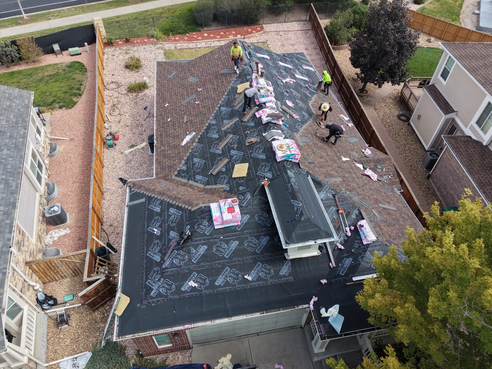 The same brick home with new brown shingles going on, crew working up the slopes