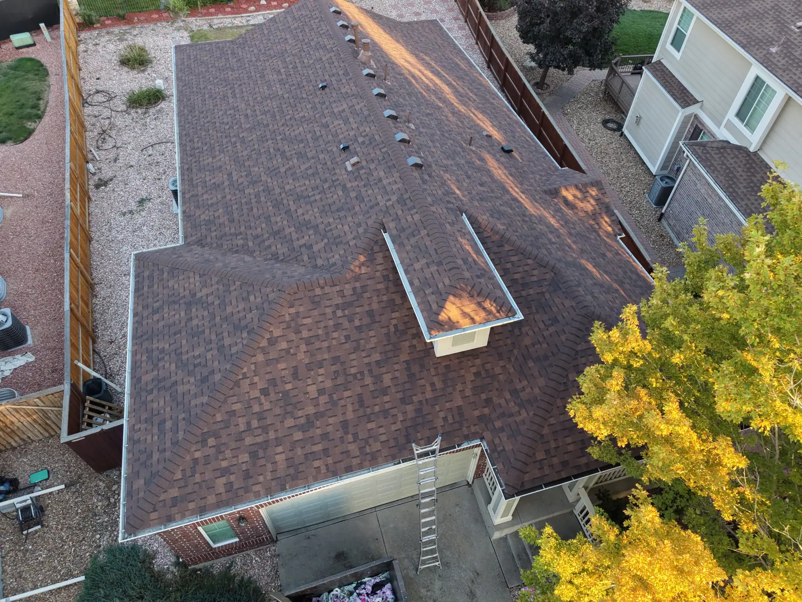 The same brick home with its finished brown shingle roof in evening light
