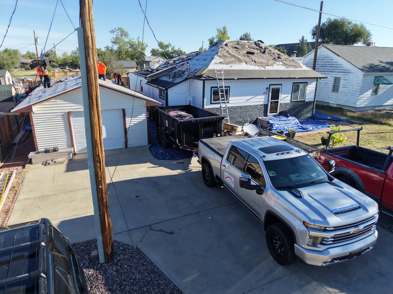 Tear-off underway on a ranch home and detached garage, AXEL Roofing truck and dump trailer in the driveway